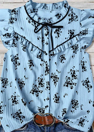 Light blue blouse with black floral pattern on a wooden surface