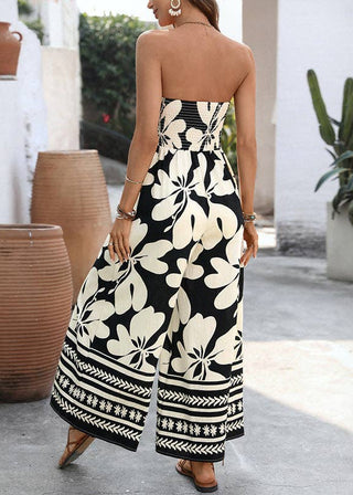 Woman wearing a black and white floral jumpsuit  in an outdoor setting with plants and vases.