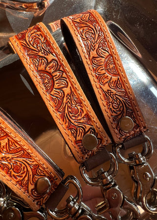 Brown leather strap with intricate patterns and metal clasps on a reflective surface