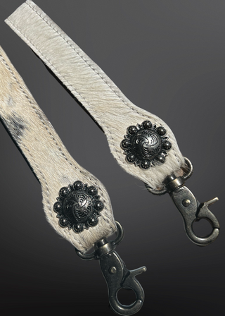 Two beige leather straps with decorative black flower clips on a dark background