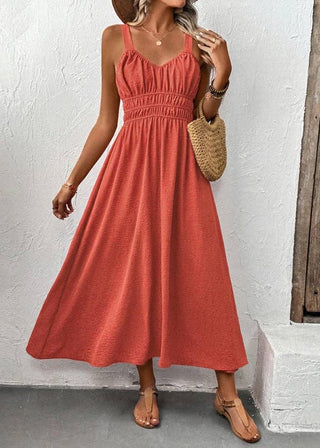 Woman wearing a coral dress standing against a white wall.