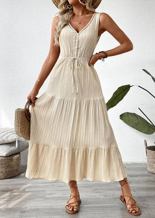 Woman wearing a beige dress holding a straw bag in a room with plants and furniture.