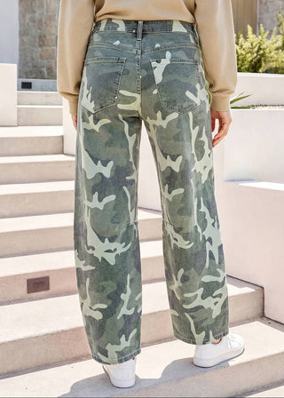 A person wearing camouflage wide-leg jeans, a beige long-sleeve top, and white sneakers, standing on outdoor concrete steps.