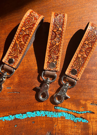 Three leather straps with intricate patterns on a wooden surface.