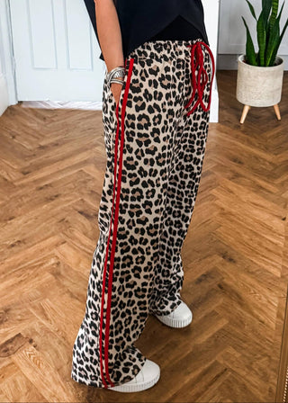 Person wearing leopard print pants with red stripes on a wooden floor.