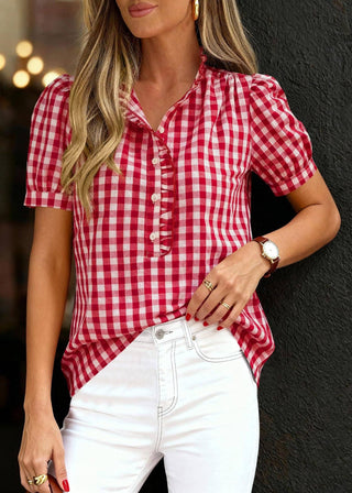 Woman wearing a red and white checkered shirt with white pants against a dark background
