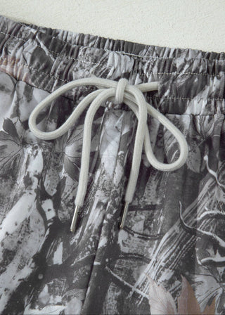 Close-up of a pair of shorts with a gray, white, and black abstract floral print and a matching light gray drawstring.