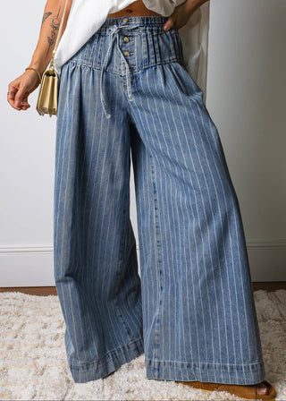 Person wearing blue wide-leg jeans and a white top, standing on a light-colored rug.