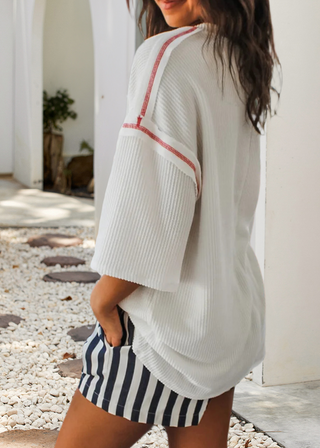 Woman wearing a white ribbed top with bold blue “USA” lettering and red stitching