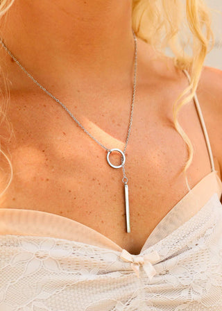 Necklace with circular and bar pendants worn by a person with blonde hair.