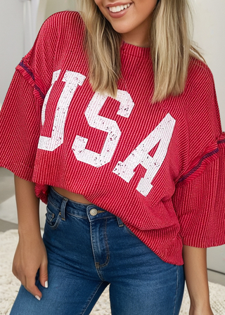 Woman wearing a red ribbed top with bold white “USA” lettering and red stitching