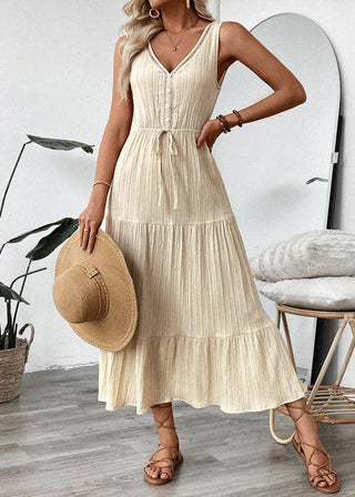 Woman in a beige dress holding a straw hat in a room with a plant and round mirror.