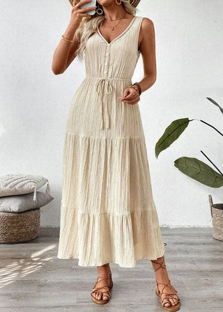 Woman wearing a beige dress standing in a room with a plant and cushions.