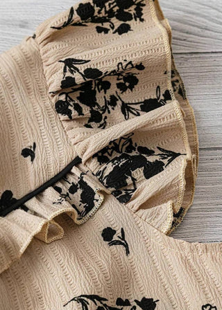 A close-up of a beige textured garment with black floral and bird silhouettes, laid on a whitewashed wood surface.