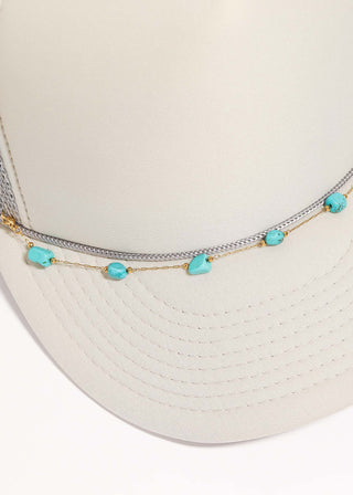 White trucker's hat with turquoise beads and gold chain on a white background