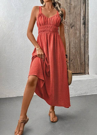 Woman wearing a coral dress standing against a white wall with a wooden door.