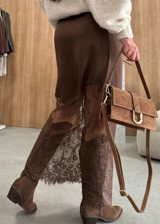 Person wearing brown boots and holding a brown handbag in a room with wooden walls and a beige chair.