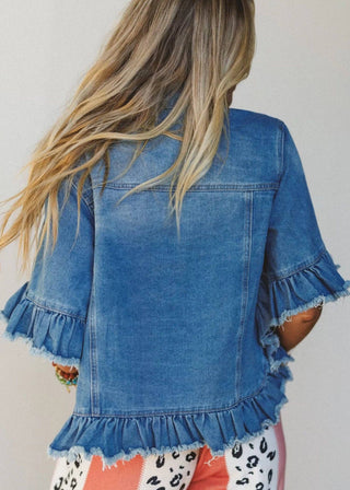 Person wearing a blue denim jacket with ruffled edges on a plain background