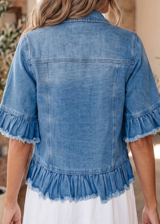 Blue denim jacket with ruffled hem worn by a person, blurred background