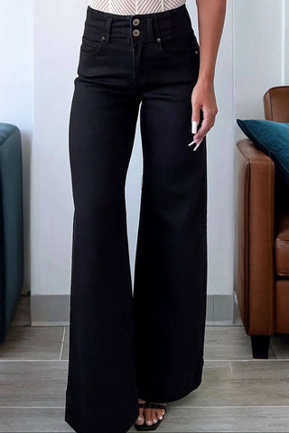 Woman wearing a white top and black flared pants in a living room setting.